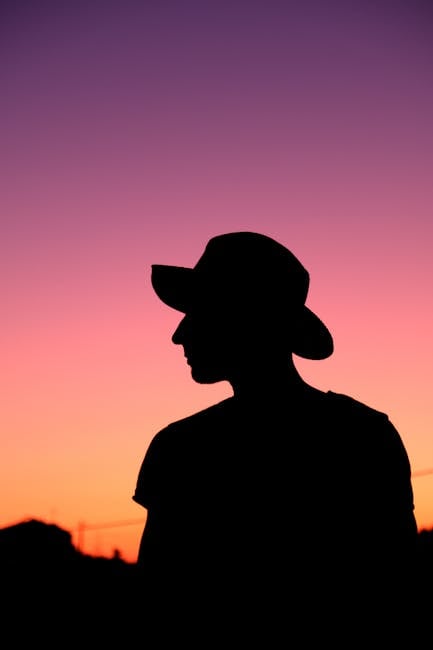 Dramatic silhouette of a person wearing a hat against a vibrant sunset sky in Portugal.
